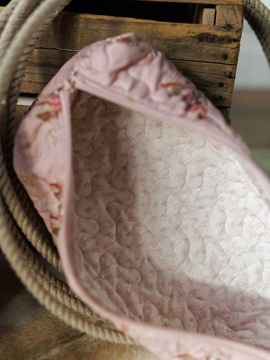 A close-up of the Brumby Rose Collection quilted bag by Savannah Sevens western life{&}style, light pink with a delicate pink floral interior, shown open next to a thick rope and wooden crate.