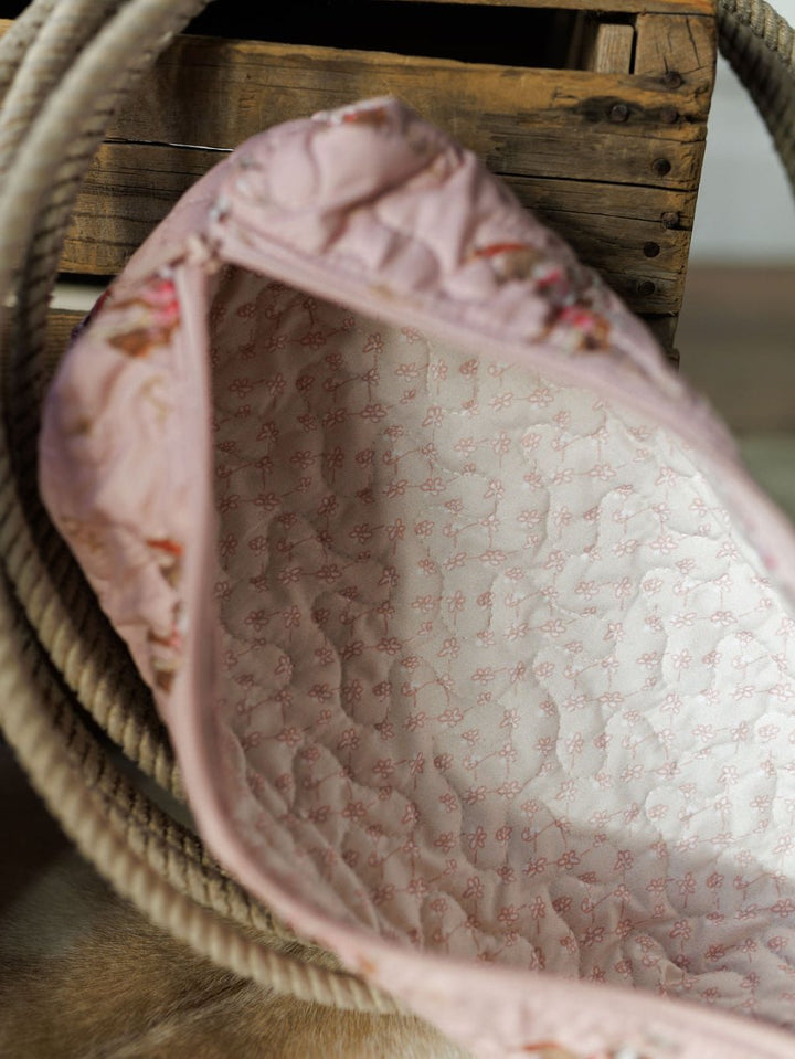 A close-up of the Brumby Rose Collection quilted bag by Savannah Sevens western life{&}style, light pink with a delicate pink floral interior, shown open next to a thick rope and wooden crate.