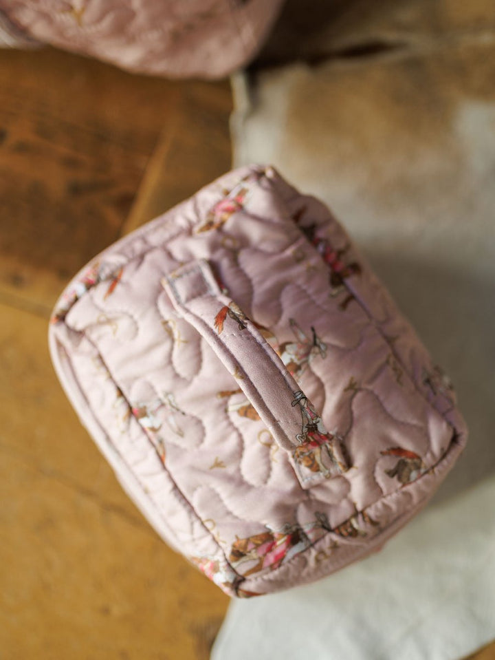 The Brumby Rose Collection by Savannah Sevens western life&style—a pink quilted bag set with a top handle and floral pattern—rests on a wooden surface beside a light-colored rug.