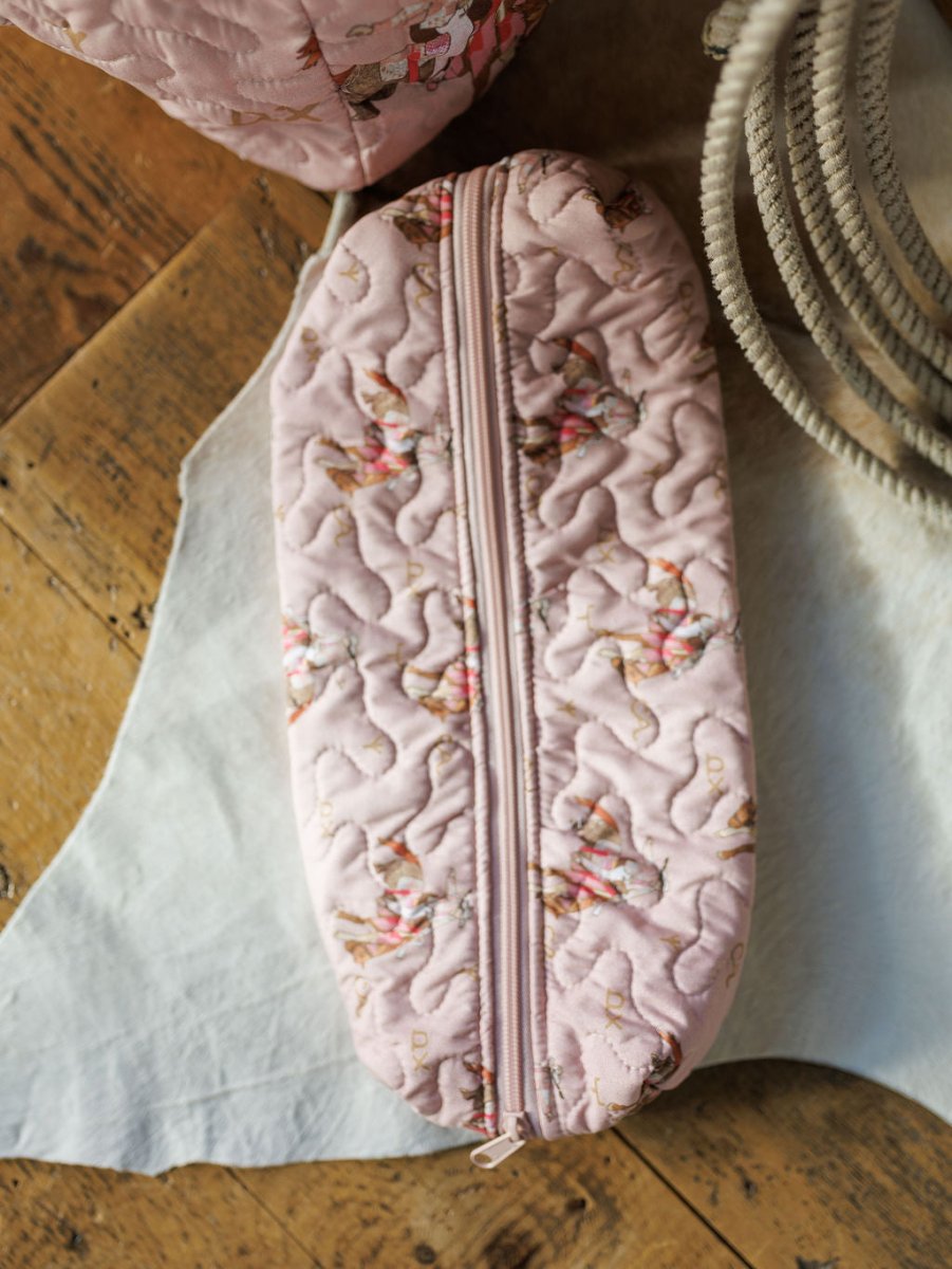 The Brumby Rose Collection pink quilted pouch by Savannah Sevens western life & style, featuring a floral pattern and zipper closure, is displayed on a white cloth atop a wooden floor.