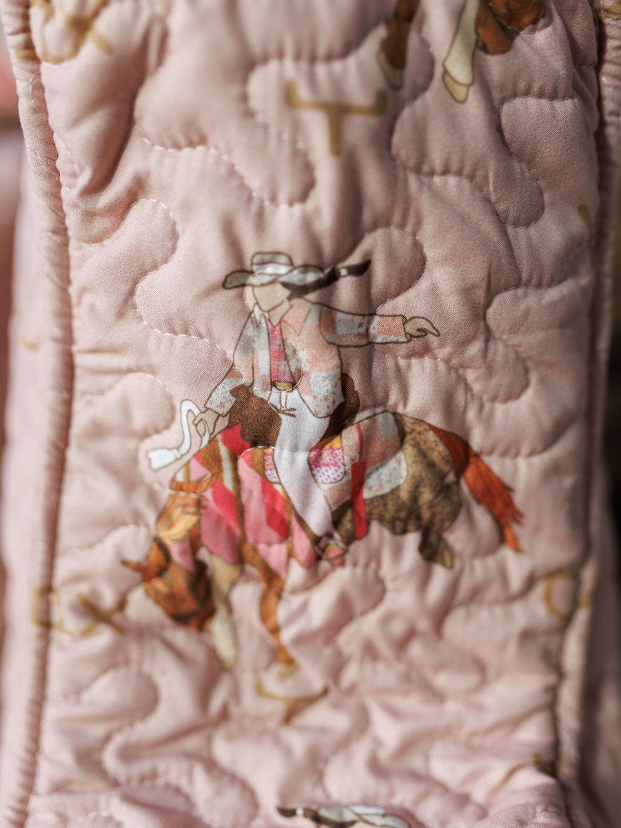 Close-up of quilted pink fabric from the Brumby Rose Collection by Savannah Sevens western life{&}style, featuring a cowboy-on-horse print with intricate stitching in soft brown, beige, and red tones.