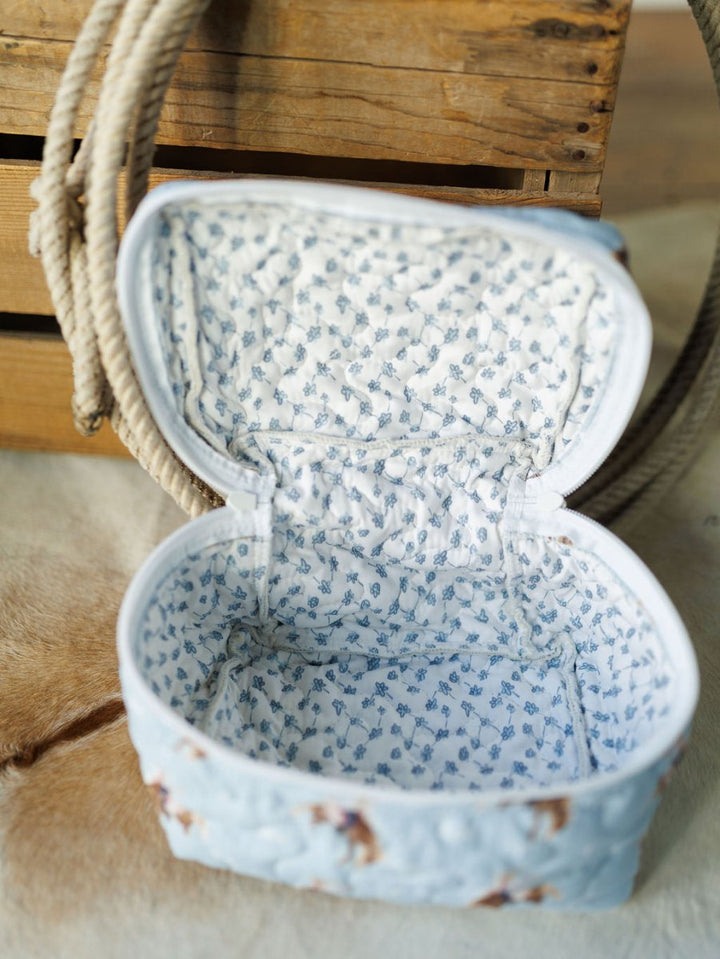 A small, fabric-lined open pouch with a blue floral pattern from the Brumby Sky Collection by Savannah Sevens western life{&}style sits in front of a wooden crate and coiled rope on a soft, tan surface. By Ida Mae. 
