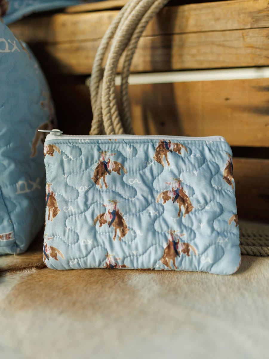 The Brumby Sky Collection quilted pouch by Savannah Sevens western life{&}style features a light blue rodeo cowgirl pattern, shown on wood with rope and a matching Brumby Sky piece in the background. By Ida Mae. 