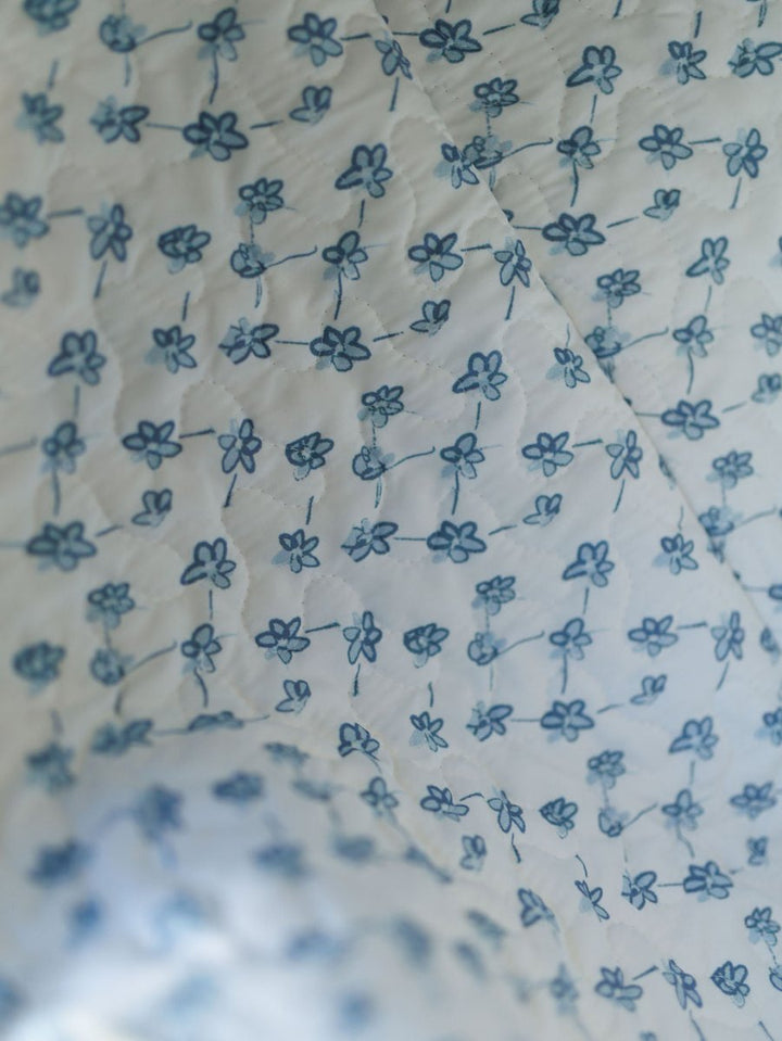 A close-up of white fabric with small blue flowers linked by dotted lines, offering a delicate vintage look—ideal for a quilted bag set from the Brumby Sky Collection by Savannah Sevens western life&style. By Ida Mae. 