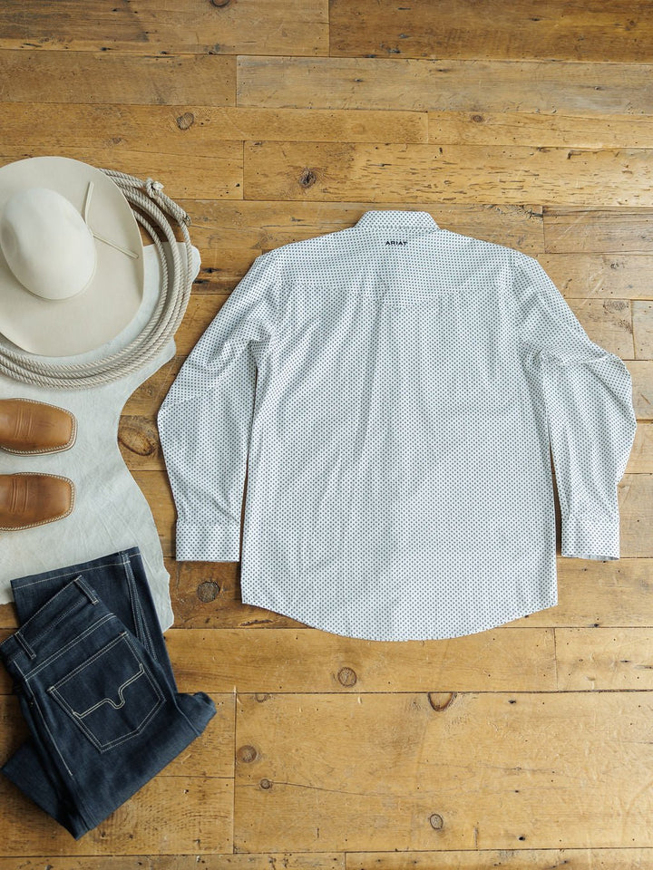 The Burke Ariat Men's Southwest Pearl Snap shirt by Savannah Sevens western life{&}style is laid flat on a wooden floor alongside a white cowboy hat, brown boots, and folded blue jeans.