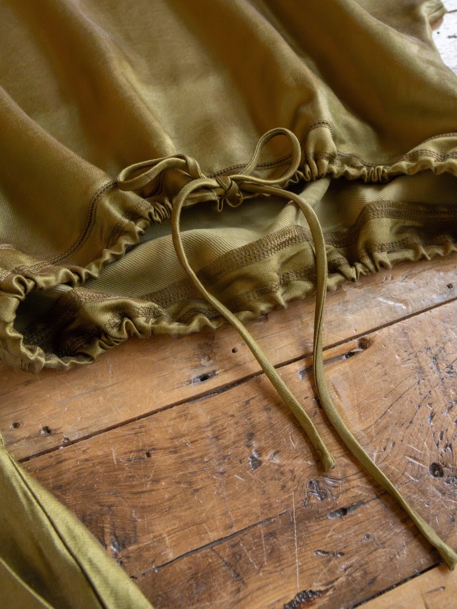 A close-up of the Savannah Sevens western life{&}style Caddo Olive Satin Set, featuring a tri-blend top with a ruched hem and adjustable drawstring, laid flat on rustic wood—perfectly paired for chic style.