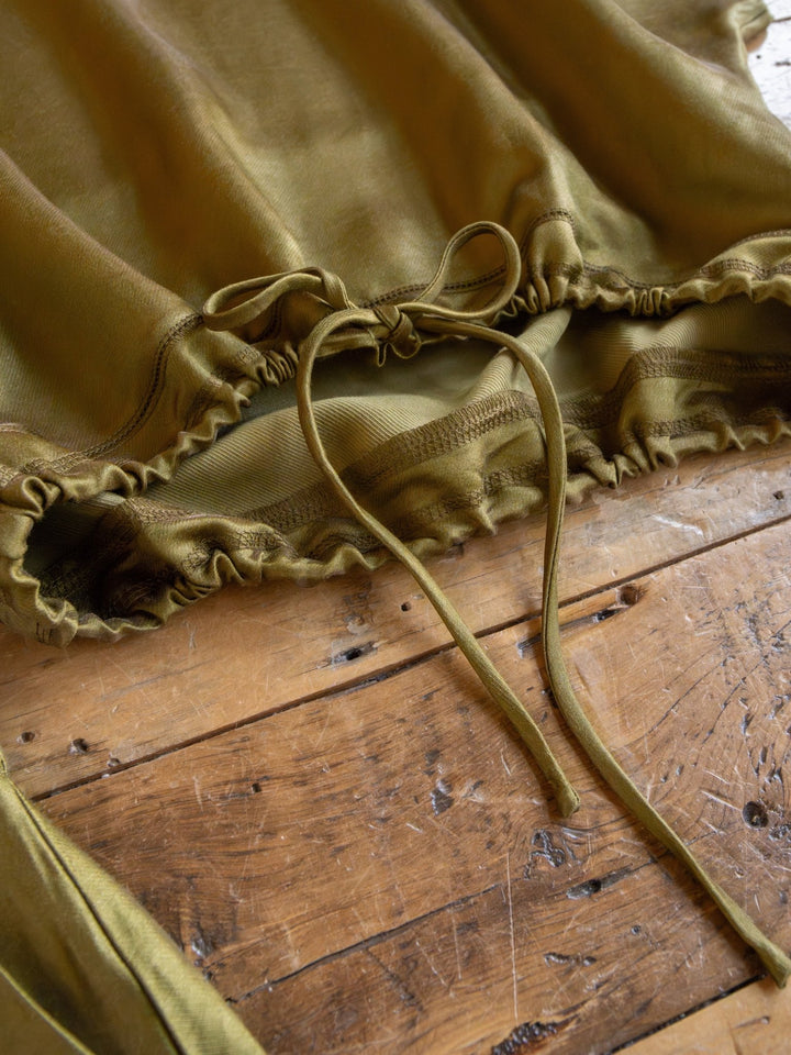 A close-up of the Savannah Sevens western life{&}style Caddo Olive Satin Set, featuring a tri-blend top with a ruched hem and adjustable drawstring, laid flat on rustic wood—perfectly paired for chic style.