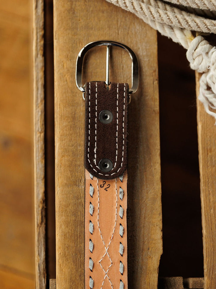 A close-up of the Camargo Belt by Savannah Sevens western life{&}style, featuring rough out leather, white stitching, a sterling silver buckle, and size 32 marked on it, resting on wood with coiled rope in the background.
