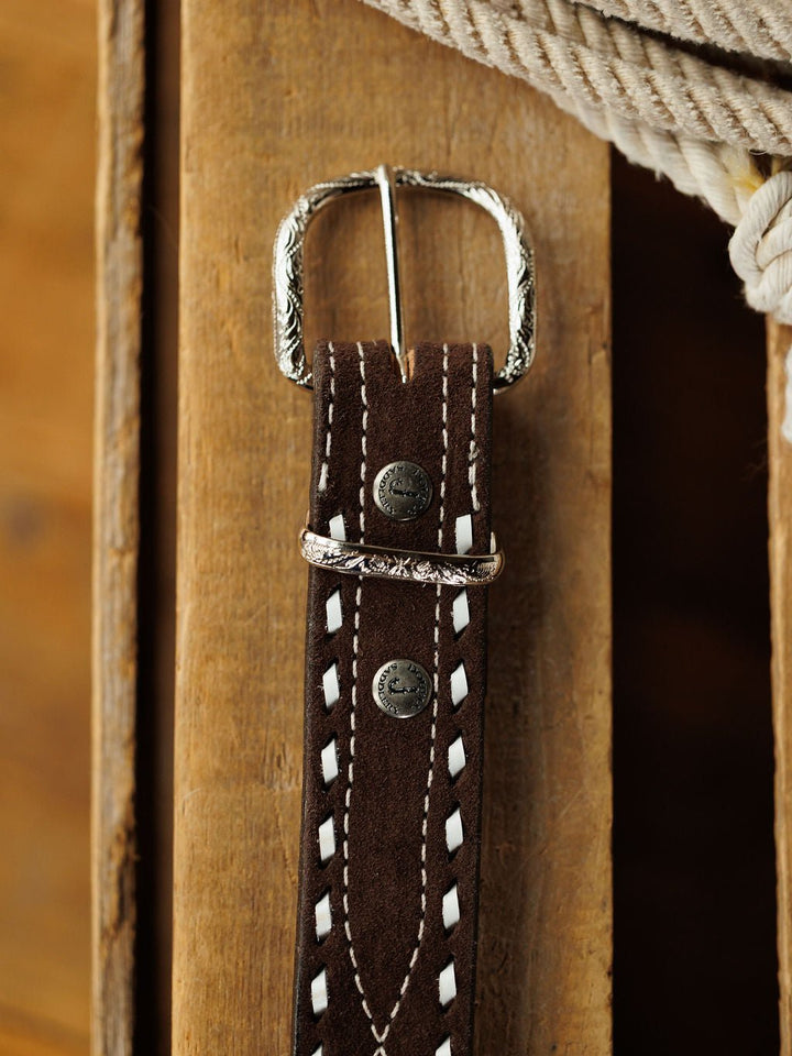 A close-up of the Camargo Belt by Savannah Sevens western life{&}style, crafted from rough out leather with white stitching and a sterling silver buckle, resting on wood with coiled rope in the background.