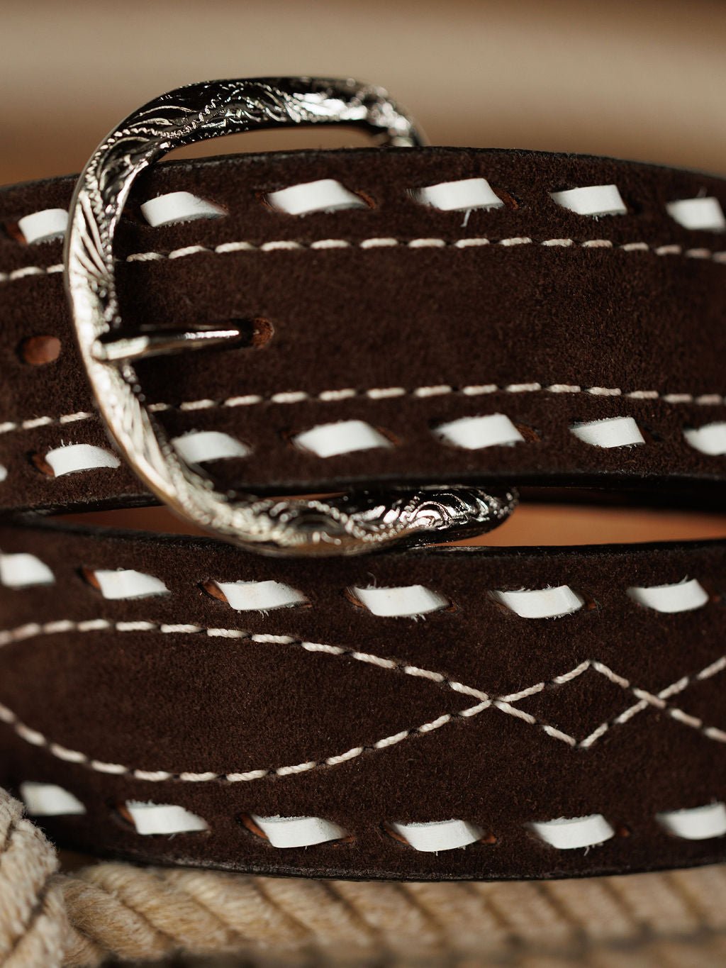 Close-up of the Camargo Belt by Savannah Sevens western life{&}style, crafted from brown rough out leather with white stitching, decorative patterns, and an ornate engraved sterling silver buckle.