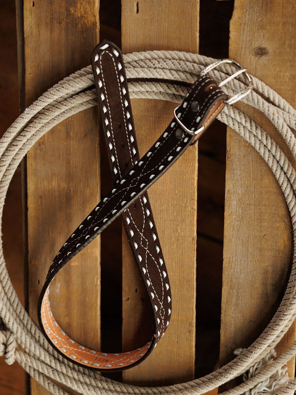 The Camargo Belt by Savannah Sevens western life{&}style, crafted from brown rough out leather with white stitching, is displayed diagonally across a coiled rope on wood, forming an X.