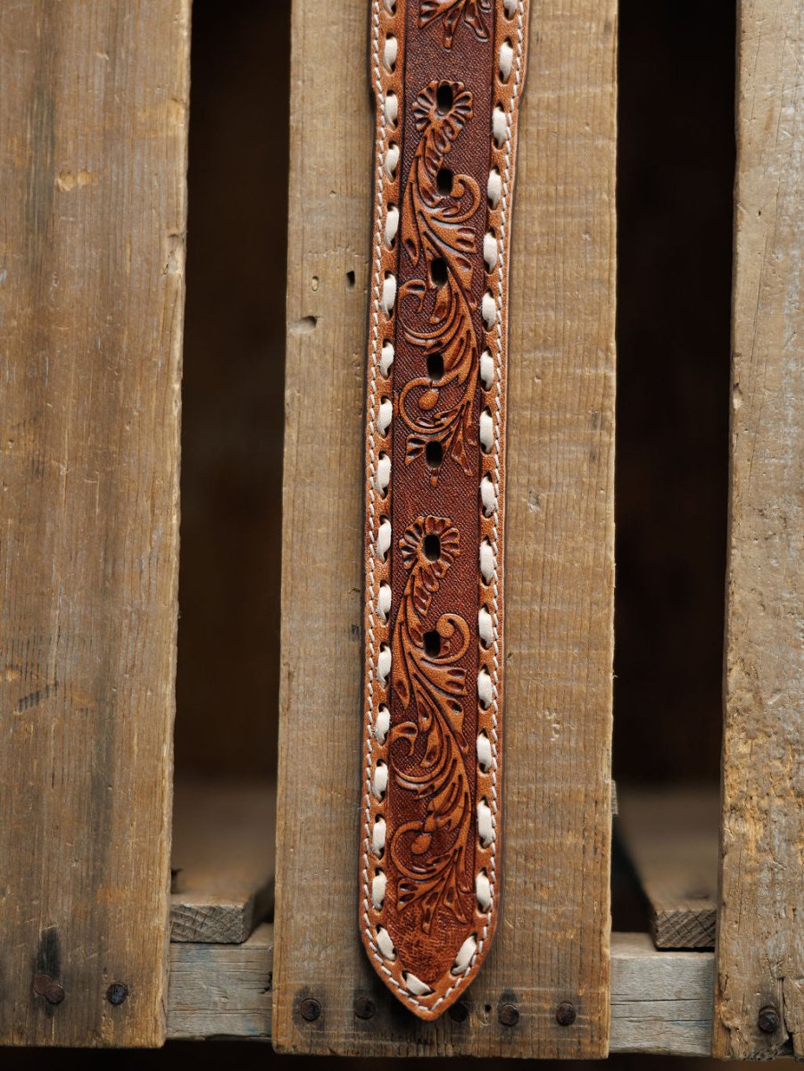 A close-up of the Camarillo Belt by Savannah Sevens western life{&}style, featuring intricate floral tooling and white edge stitching, shown against a rustic wooden background.