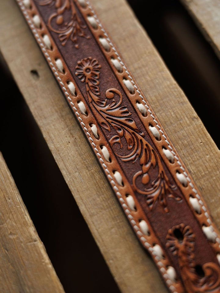 A close-up of the Camarillo Belt by Savannah Sevens western life{&}style, featuring intricate floral tooling and decorative stitching, displayed on a wooden slatted surface.