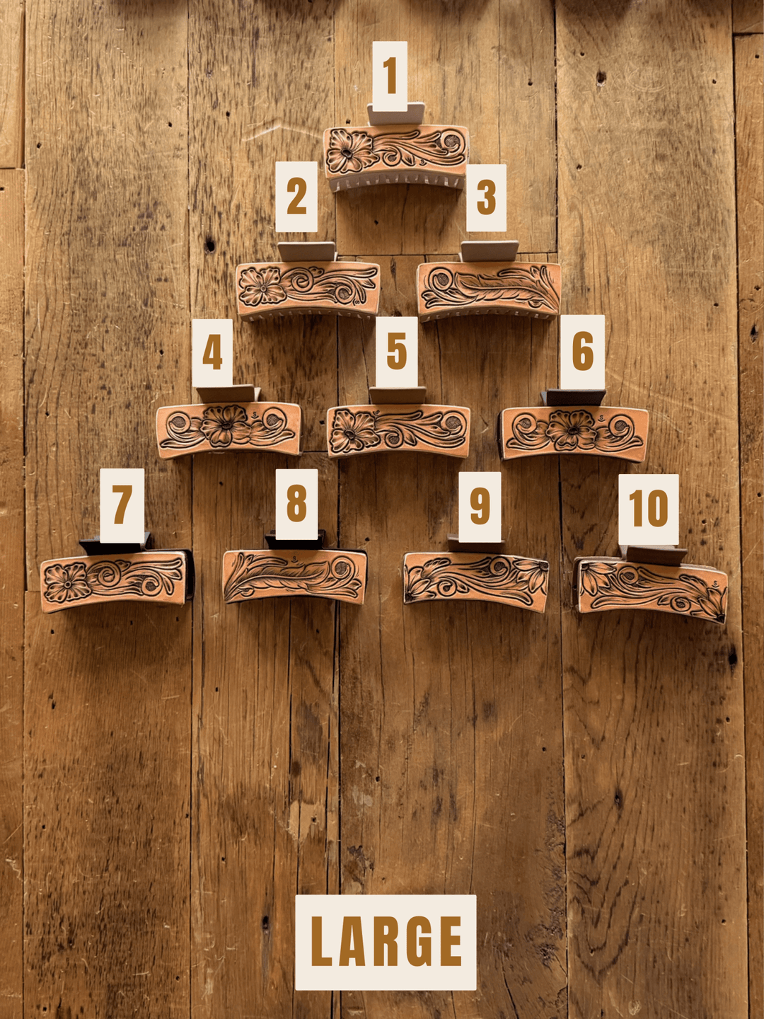 Ten unique hand-tooled leather Campitos Claw Clips from Savannah Sevens western life&style arranged in a pyramid on a wooden surface, each labeled with a number from 1 to 10.