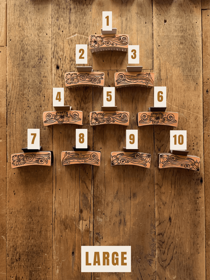 Ten unique hand-tooled leather Campitos Claw Clips from Savannah Sevens western life&style arranged in a pyramid on a wooden surface, each labeled with a number from 1 to 10.