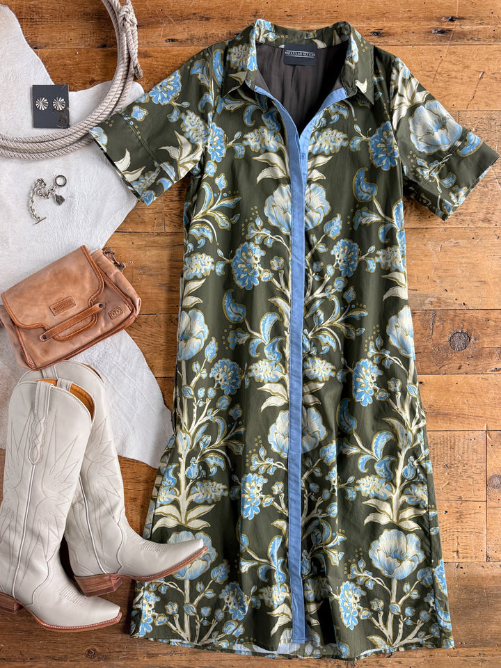 Castell Olive Floral Dress by Savannah Sevens western life{&}style styled with white cowboy boots, a tan leather bag, silver necklace, and earrings, all arranged on a wooden floor.