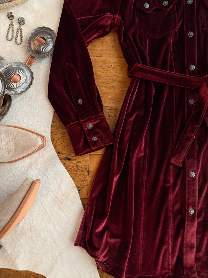 The Centralia Wine Velvet Button Up Dress by Savannah Sevens western life{&}style is styled with brown cowboy boots, silver jewelry, and a white cowhide rug—an ideal western yoke dress inspired by Tasha Polizzi.