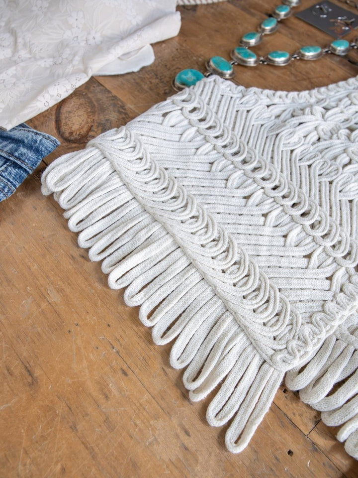 A close-up of the Cerrillo Natural Crochet Vest by Savannah Sevens western life{&}style on wood, with a turquoise beaded necklace, jeans, and floral fabric partially visible around it.