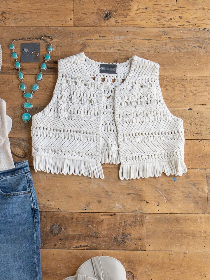 The Cerrillo Natural Crochet Vest by Savannah Sevens western life{&}style is displayed on a wooden surface with a turquoise necklace, earrings, light blue jeans, and white shoes.
