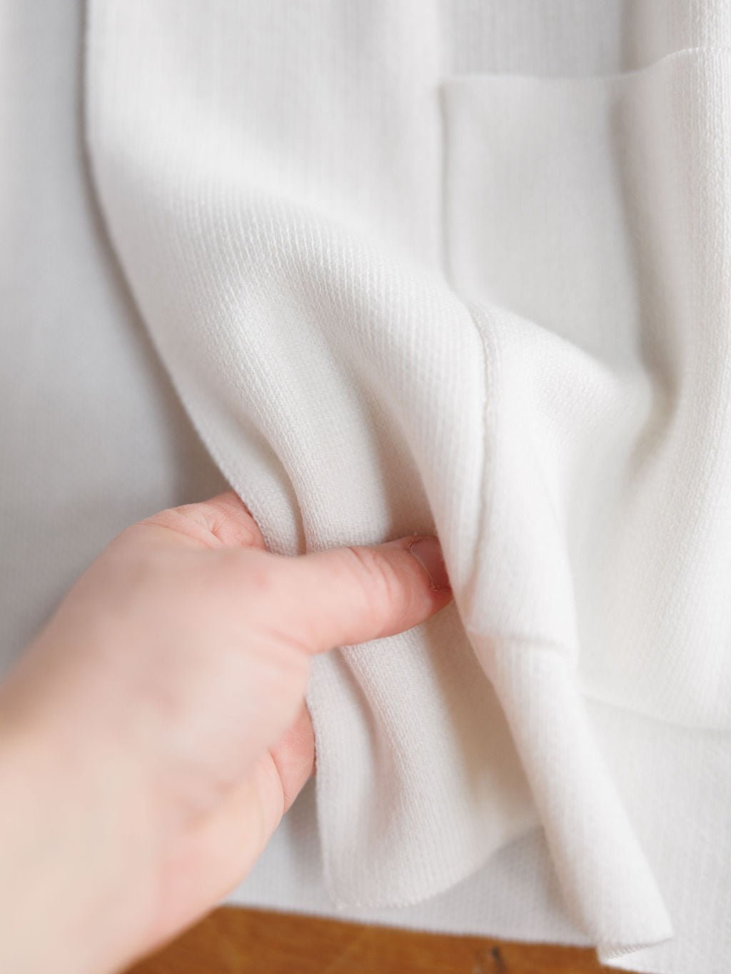 A hand gently lifts the Chamois White Cashmere Blend Cardigan by Savannah Sevens western life{&}style, highlighting its soft, ribbed texture and smooth finish against a neutral background.
