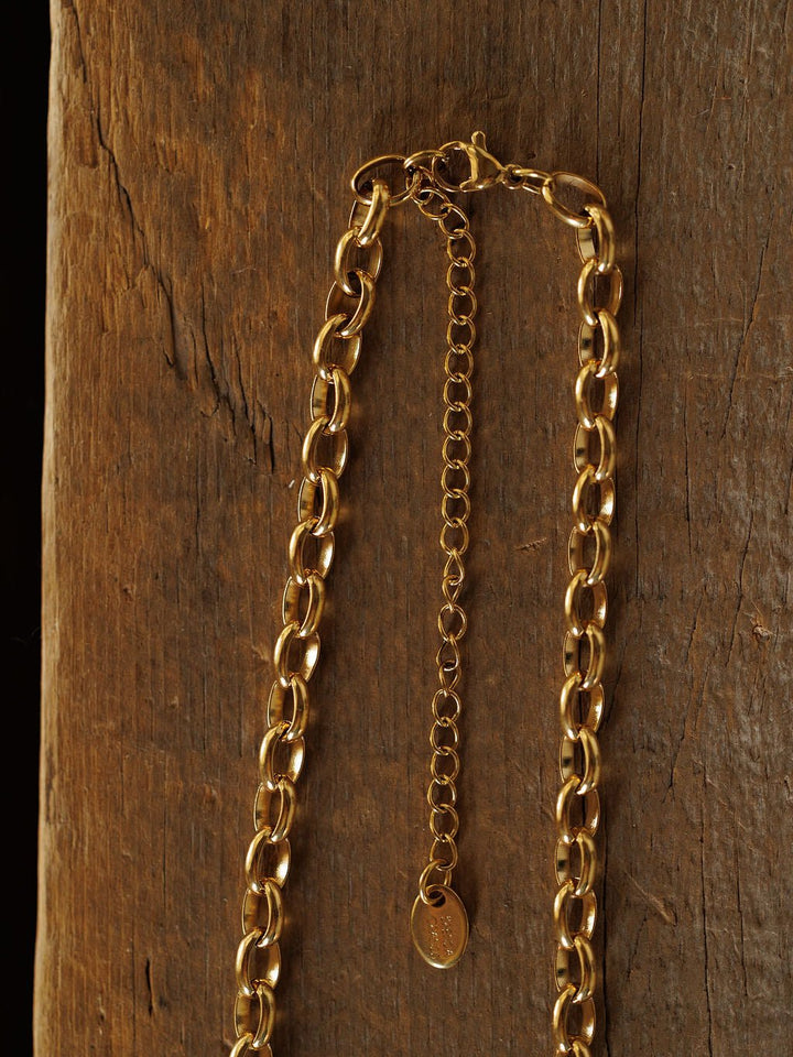 The Cheney Necklace by Savannah Sevens western life{&}style, a gold filled choker with an adjustable extender and small oval tag, is displayed on a textured wooden surface for timeless elegance.