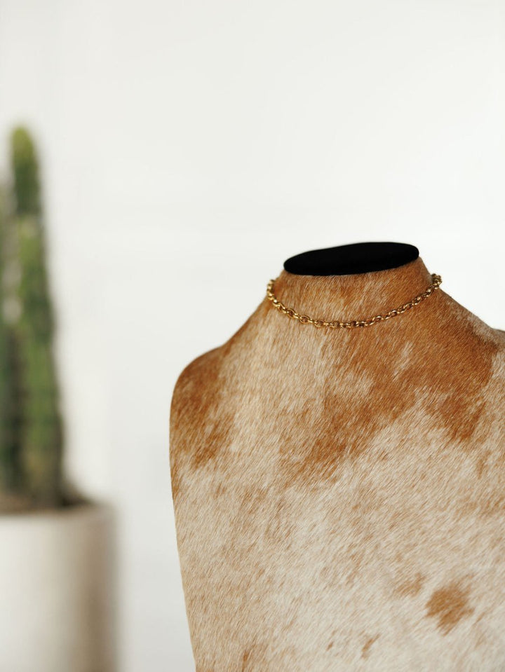 The Cheney Necklace by Savannah Sevens western life{&}style is shown on a cowhide-covered mannequin, with a blurred green potted cactus in the background.