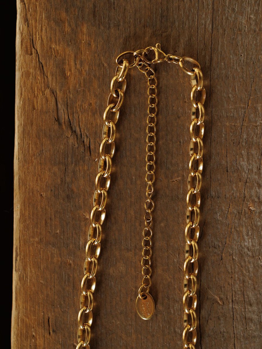 The Cheney Necklace by Savannah Sevens western life{&}style, a gold filled choker with an adjustable extender and small oval tag, is displayed on a textured wooden surface for timeless elegance.