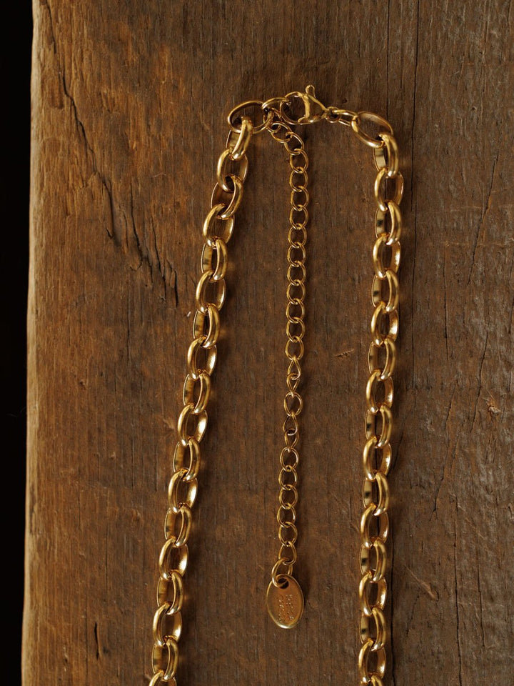 The Cheney Necklace by Savannah Sevens western life{&}style, a gold filled choker with an adjustable extender and small oval tag, is displayed on a textured wooden surface for timeless elegance.