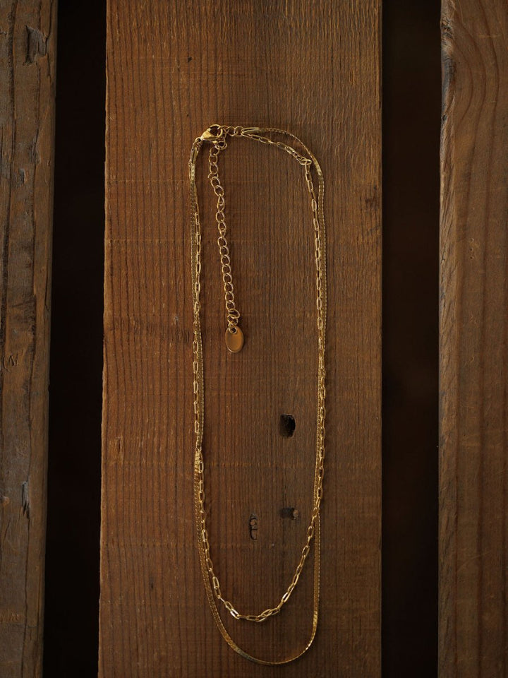 The Chenoa Necklace by Savannah Sevens western life{&}style features a delicate, hypoallergenic 18K gold filled chain and adjustable clasp, adding subtle elegance to any outfit. Displayed vertically against a rustic brown wooden background.