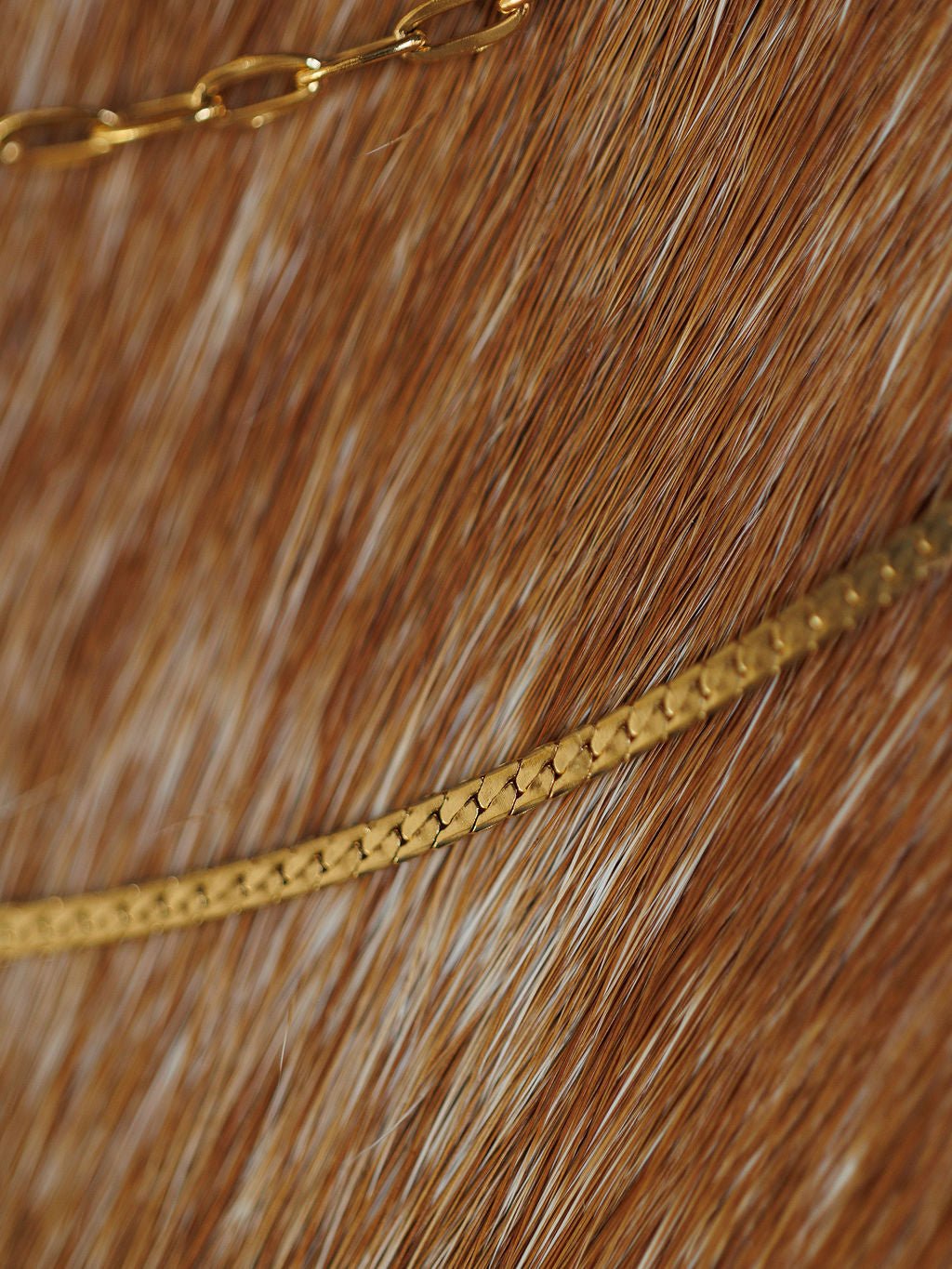 Close-up of two Savannah Sevens western life{&}style Chenoa Necklaces, featuring 18K gold filled chains gently curving over a brown and white fur surface.