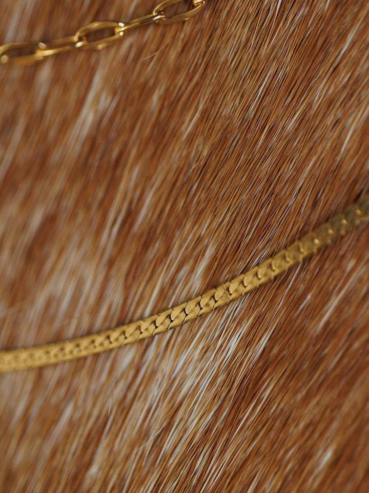 Close-up of two Savannah Sevens western life{&}style Chenoa Necklaces, featuring 18K gold filled chains gently curving over a brown and white fur surface.