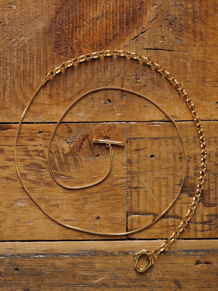 The Cheraw Necklace by Savannah Sevens western life{&}style is displayed in a loose spiral on rustic wood, highlighting its detailed gold-filled chain links and clasp.