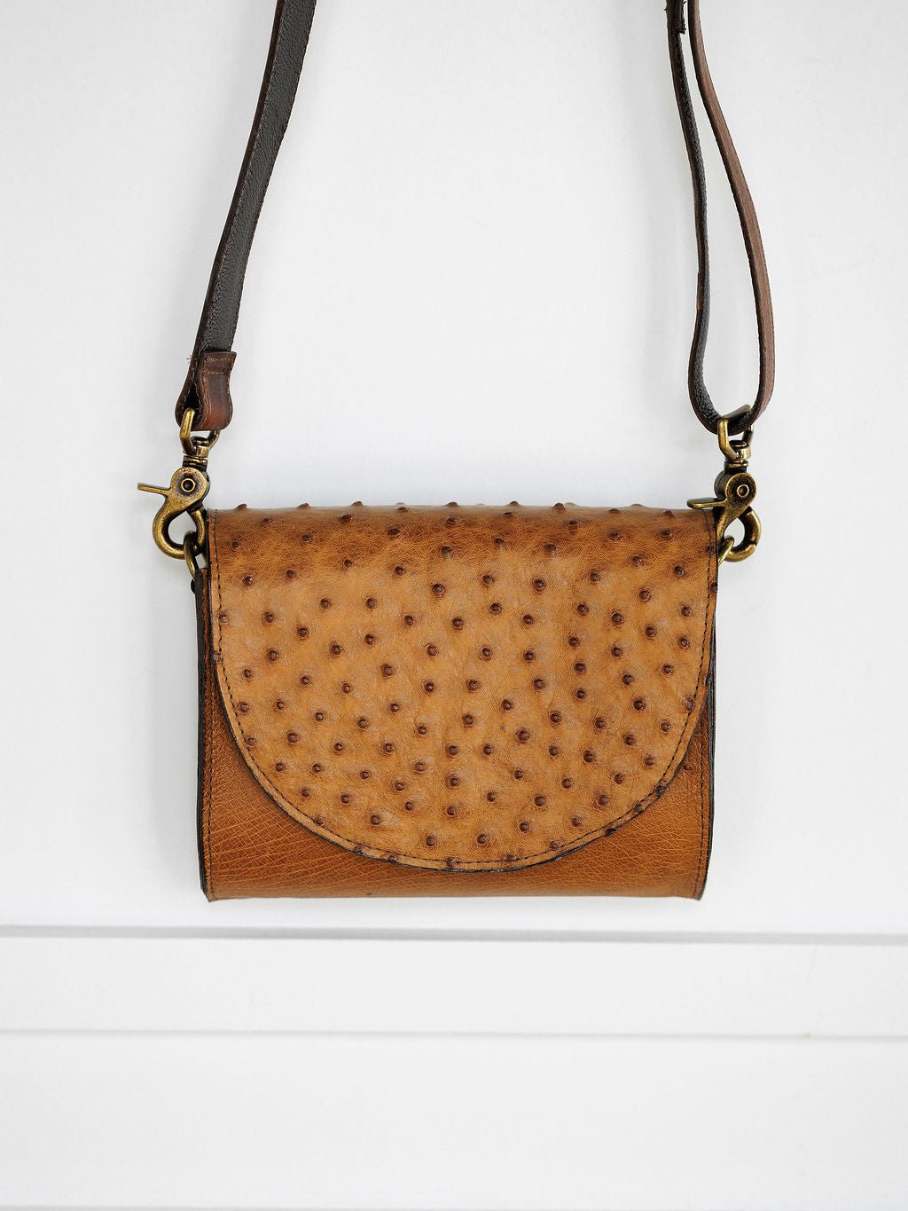 The Chicota Ostrich Leather Crossbody Clutch by Savannah Sevens western life{&}style features a small brown ostrich leather design with a dimpled flap and dark adjustable shoulder strap, displayed against a white background.