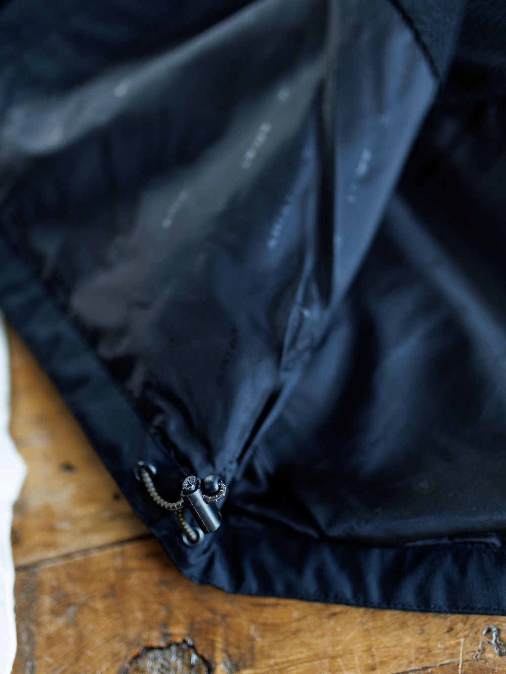 Close-up of the Collbran Ariat Men's Black Jacket by Savannah Sevens western life{&}style, showing its inner lining with a drawstring and plastic toggles, displayed on a wooden surface.