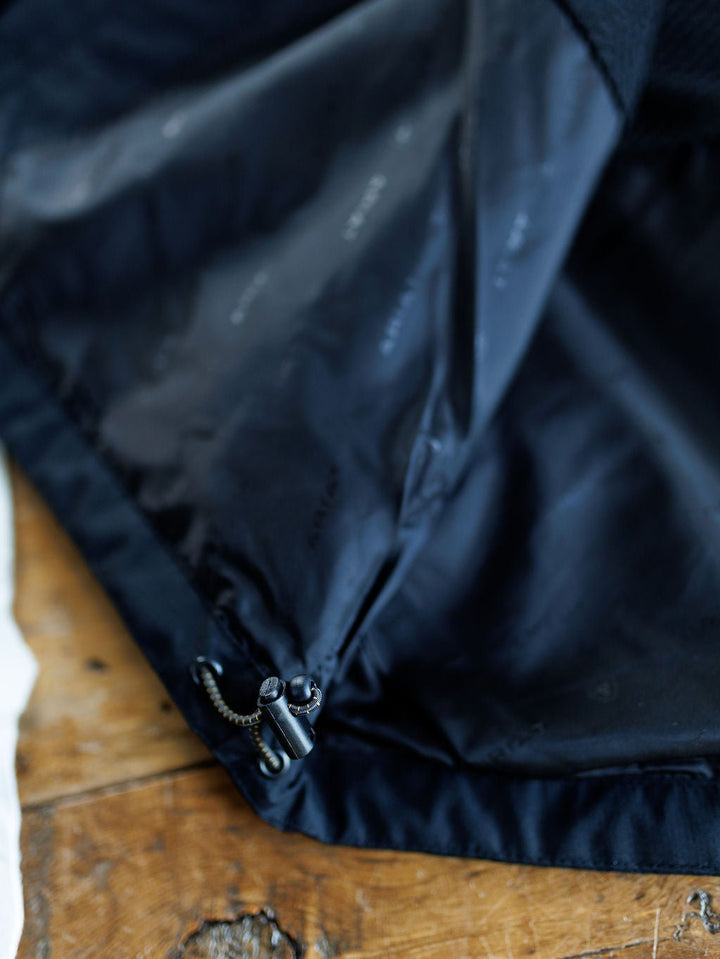 Close-up of the Collbran Ariat Men's Black Jacket by Savannah Sevens western life{&}style, showing its inner lining with a drawstring and plastic toggles, displayed on a wooden surface.