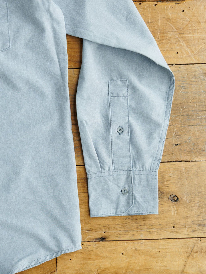 The Colman men's snap button shirt by Savannah Sevens western life&style, in light blue with long sleeves and buttoned cuffs, is displayed flat on wood, highlighting its moisture wicking and UV protection features.