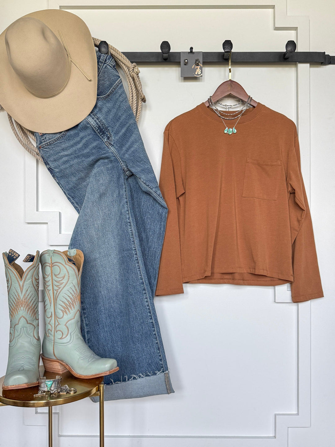 A Western outfit featuring the Colville Caramel Basic Top by Savannah Sevens western life{&}style, styled with a tan hat, blue jeans, turquoise cowboy boots, and turquoise jewelry, displayed on a white wall and wooden stool.