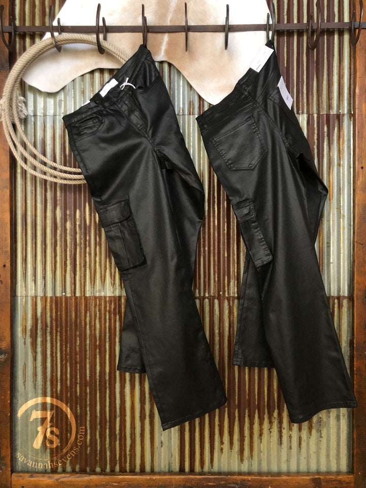 Two pairs of The Conrad High Rise 90's Straight Leg Jeans by Savannah Sevens western life{&}style hang on hooks against a rustic metal and wood wall, with a coiled rope and light cowhide in the background for a vintage touch.