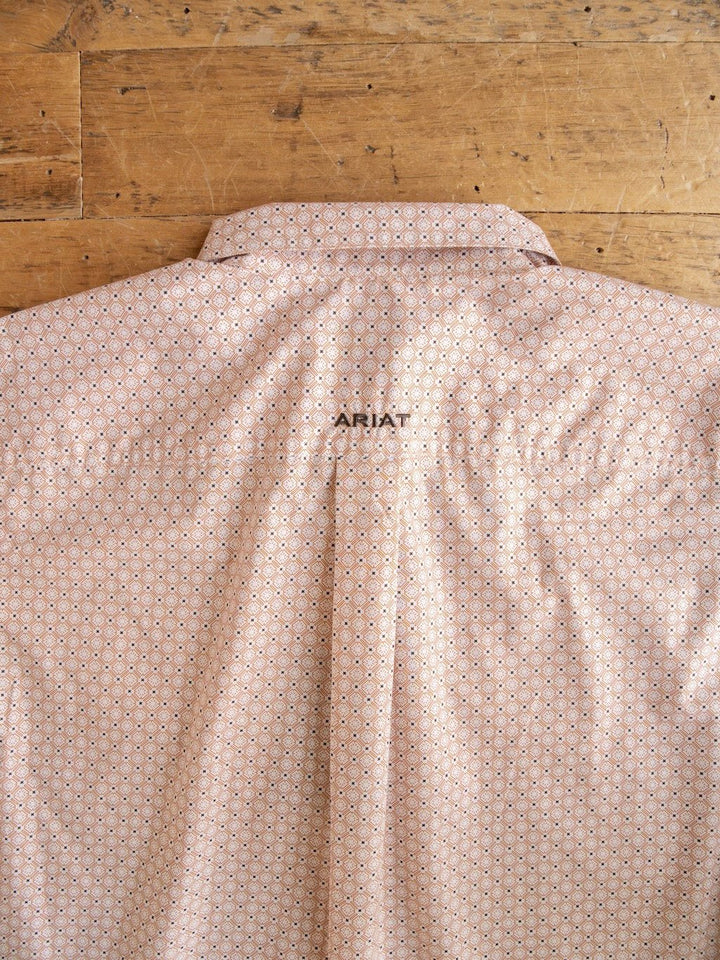 A light pink patterned Copeland Ariat Men's Southwest Button Up from Savannah Sevens western life{&}style is laid flat on a wooden surface, displaying the back with ARIAT embroidered in small black letters below the collar.