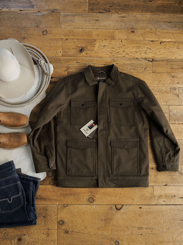 A Cornell Ariat Men’s Insulated Jacket from Savannah Sevens western life{&}style, in olive green, is laid on a wooden floor beside tan boots, folded denim jeans, a coiled rope, and a white cowboy hat. The jacket features wind and water resistance.