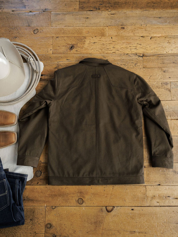 A Savannah Sevens western life{&}style Cornell Ariat Men's Insulated Jacket in brown is laid flat on a wooden floor beside a white cowboy hat, tan shoes, and dark blue jeans.