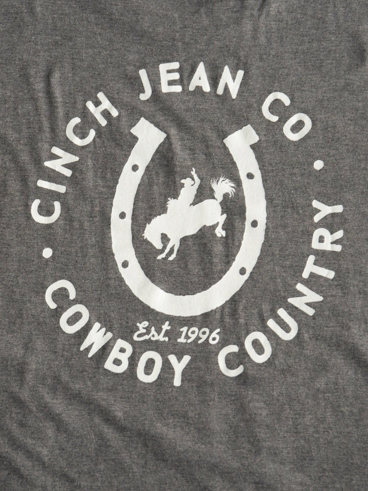 The Cowboy Country Men's Graphic Tee by Savannah Sevens western life{&}style features gray fabric, a white horseshoe, a cowboy on a bucking horse, and the text "COWBOY COUNTRY Est. 1996.