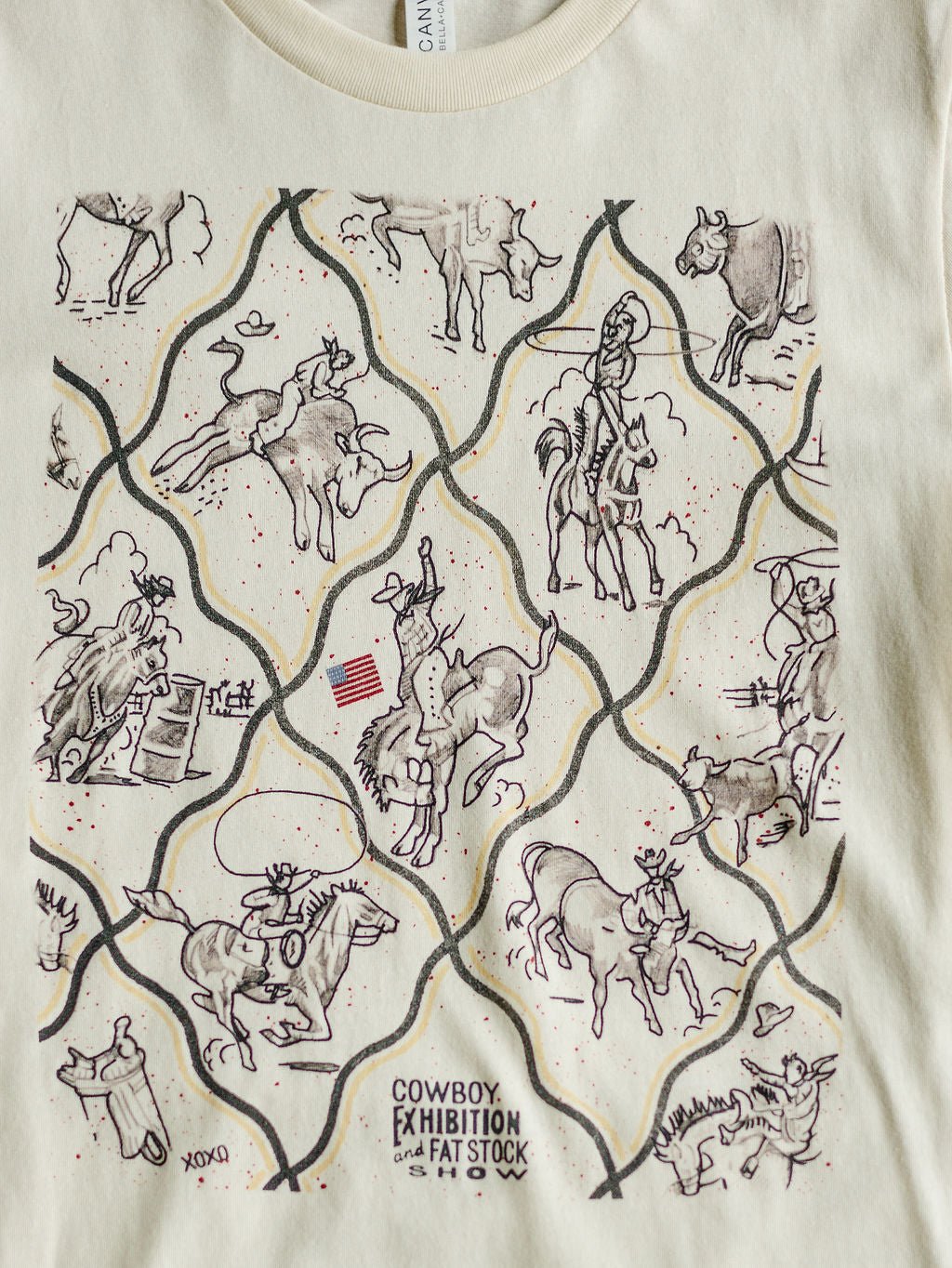 The Cowboy Exhibition tee by Savannah Sevens western life{&}style is cream-colored and features line-drawn cowboys riding bulls, roping cattle, rodeo tricks, an American flag, and the text COWBOY EXHIBITION and FAT STOCK SHOW.