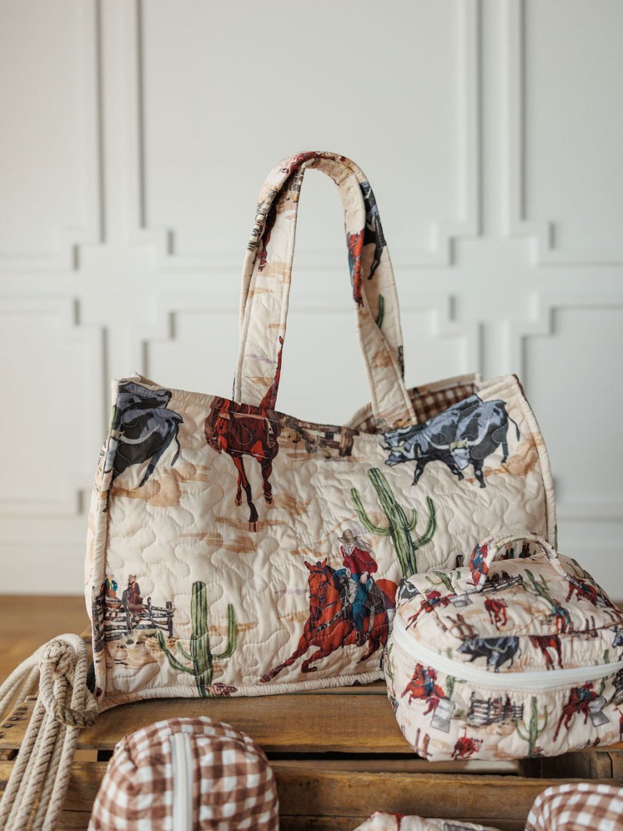 The Cowgirl Gingham {Collection} by Savannah Sevens western life{&}style features a quilted travel bag and matching case with cowboy, horse, cactus, and gingham prints, displayed on wood with other patterns against a white decorative wall.