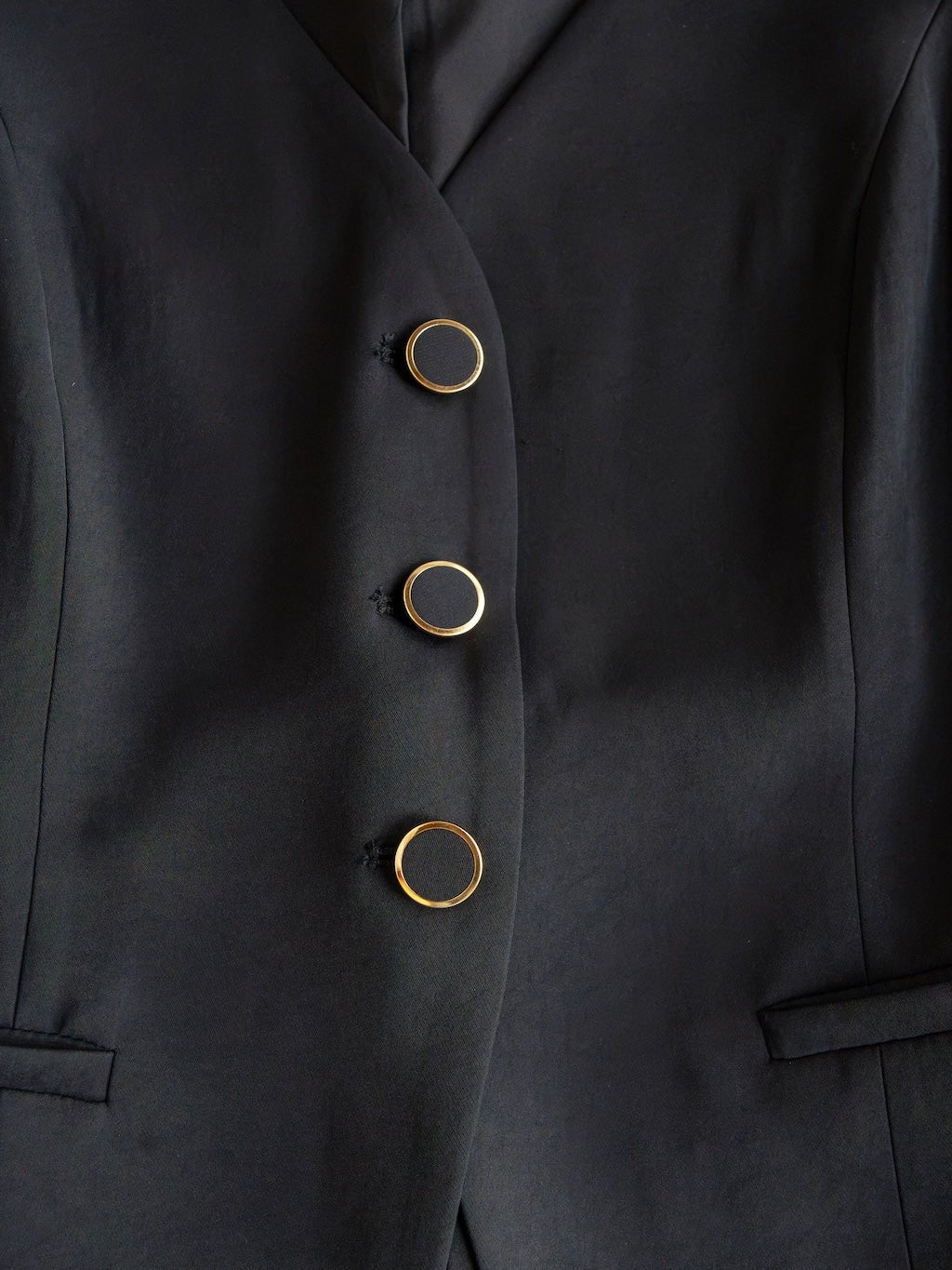 Close-up of the Cuero Black Vest Set by Savannah Sevens western life{&}style, featuring matte satin fabric, three vertically arranged black buttons with gold rims, and two horizontal front pockets.