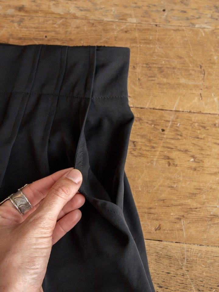 A hand wearing a silver ring holds open the pocket of the Cuero Black Vest Set by Savannah Sevens western life{&}style, revealing its matte satin lining against a wooden surface.