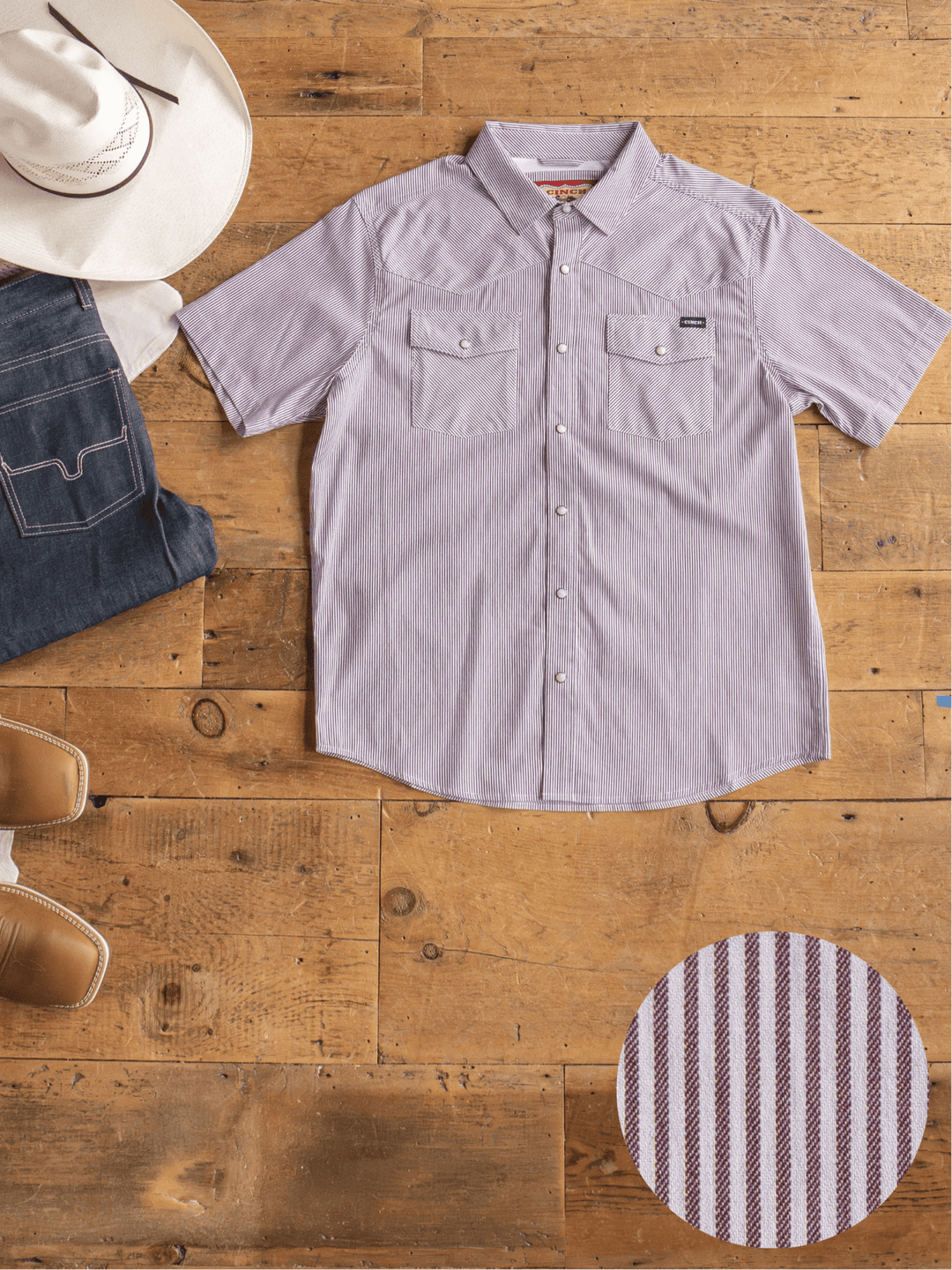 Flat lay of the Cutler Cinch Men's Pinstripe Pearl Snap by Savannah Sevens western life{&}style, folded blue jeans, a white cowboy hat, and brown cowboy boots on a wooden floor. Inset shows the shirt’s red and white stripe pattern.