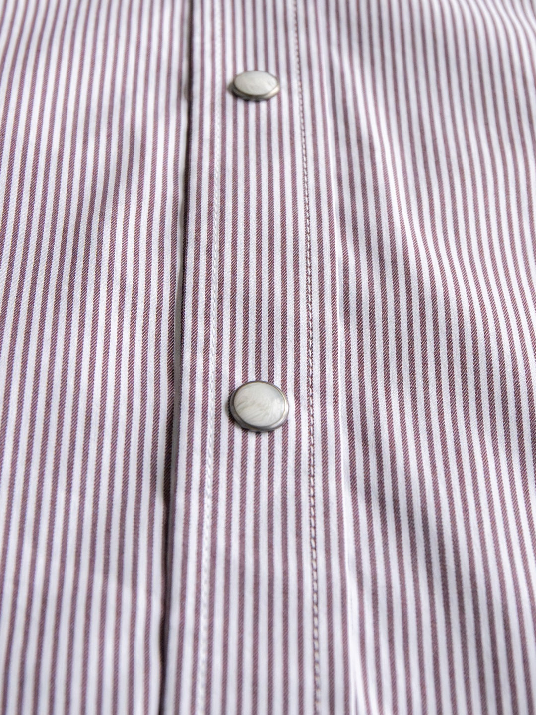 Close-up of the Savannah Sevens western life{&}style Cutler Cinch Men's Pinstripe Pearl Snap shirt, showcasing thin vertical purple and white stripes and two round pearl snap buttons on the placket.