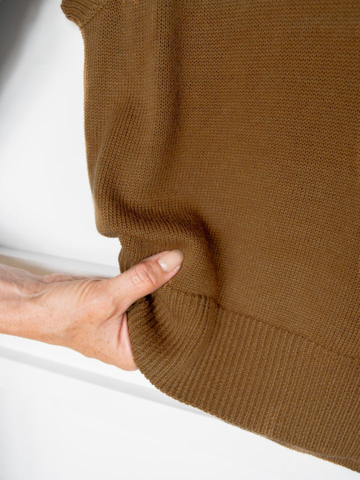 A hand pinches the bottom edge of the Dacoma Bronze Knit Top by Savannah Sevens western life{&}style, showing its wool blend fabric against a white background.