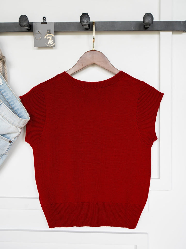 The Dacoma Cherry Red Knit Top by Savannah Sevens western life{&}style, shown on a hanger next to light blue jeans, features cap sleeves and a wool blend knit. Available in young contemporary sizing.